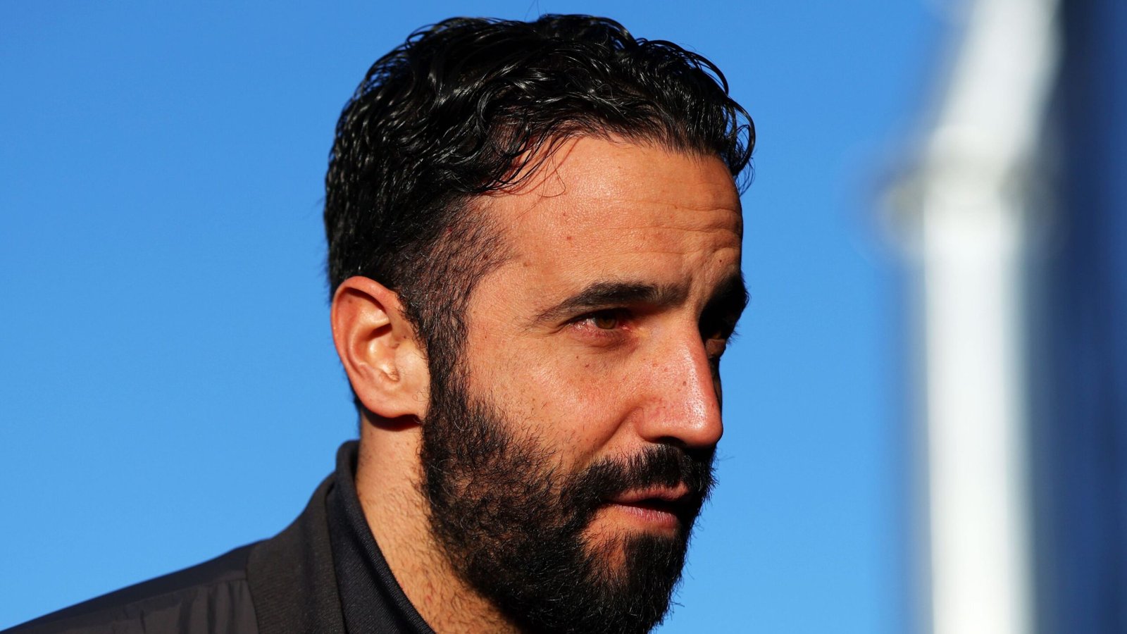 Portrait de Ruben Amorim, portant une veste sombre, avec un ciel bleu en arrière-plan, réfléchissant à son récent licenciement de Manchester United.