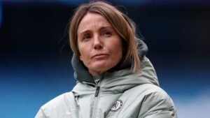 Sonia Bompastor, en survêtement de Chelsea, semble pensive après une défaite 5-1, illustrant un moment difficile pour l'équipe.