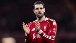 Liverpool player applauding fans in a home match, wearing the team's red kit with the club's emblem visible on the chest.