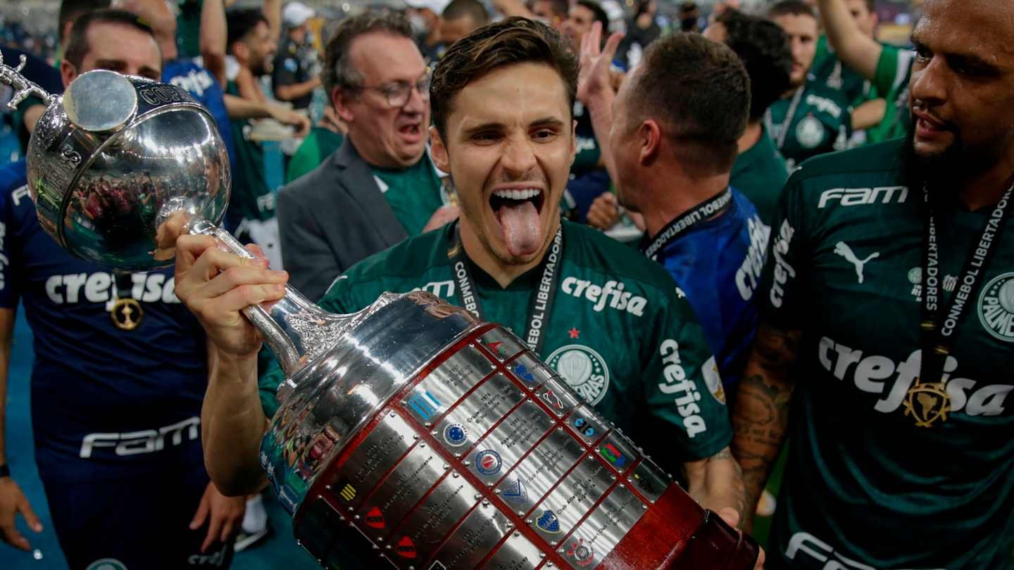 Palmeiras player celebrating with the Copa Libertadores trophy, surrounded by teammates, wearing green jerseys, joyfully expressing triumph.