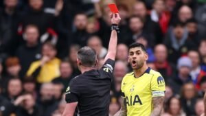 Cristian Romero, vêtu du maillot jaune de Tottenham, réagit avec incrédulité alors que l'arbitre lui montre un carton rouge pendant un match.
