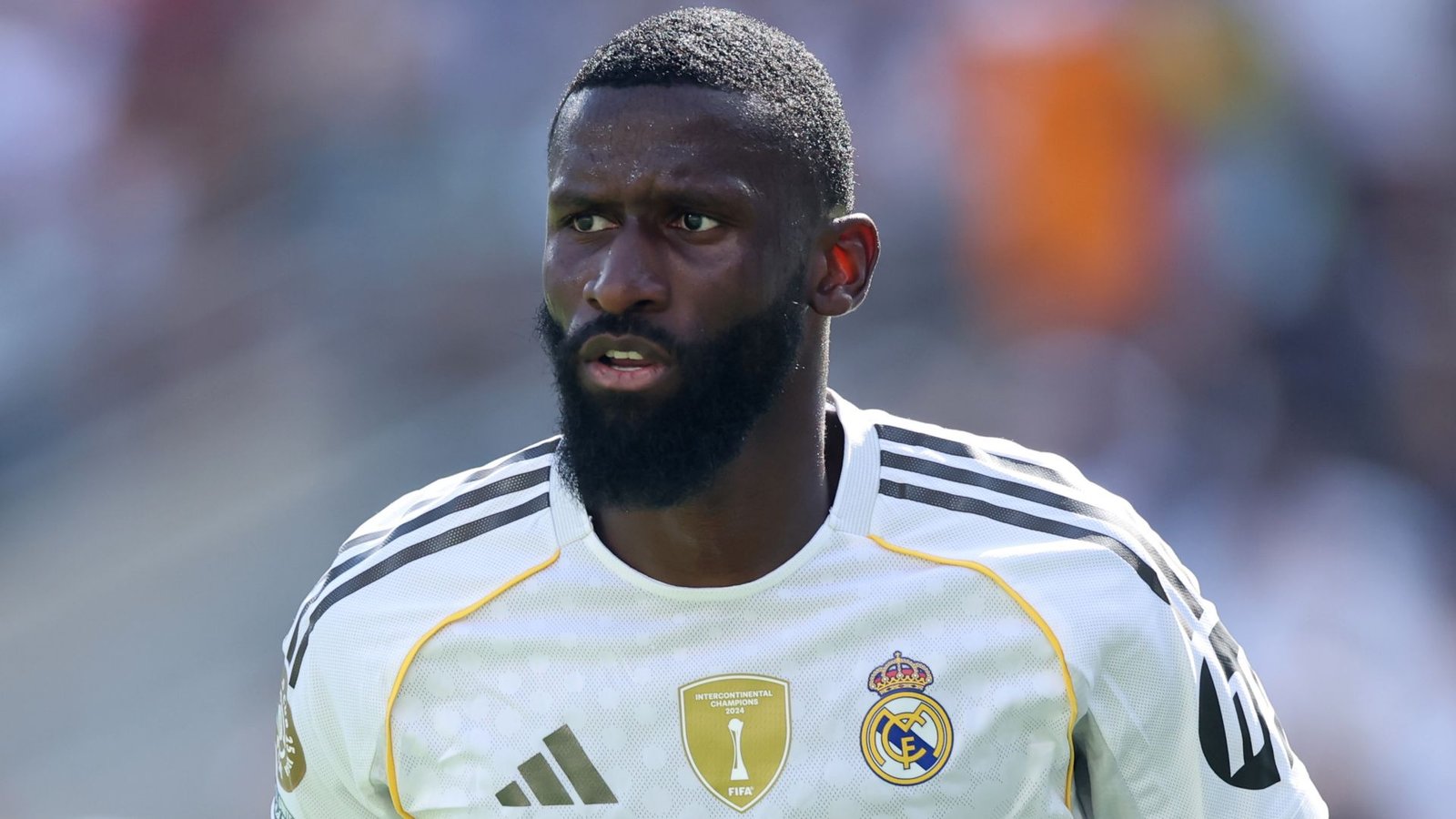 Real Madrid's Antonio Rüdiger in a white kit, focused and determined, with a distinctive beard during a match.