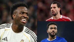Vinícius Júnior smiles while celebrating, flanked by Dominik Szoboszlai in a red kit and Reece James in blue from Chelsea.