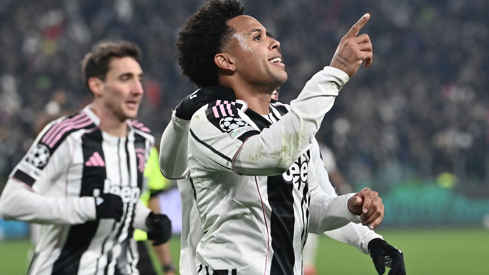 Weston McKennie célèbre en pointant le ciel dans un maillot de la Juventus aux accents roses, tandis que ses coéquipiers l'acclament lors d'un match de Ligue des Champions.