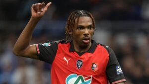 Jeremy Jacquet, in a red and black Rennes kit, gestures with his thumb up during a lively match, showcasing his enthusiasm.