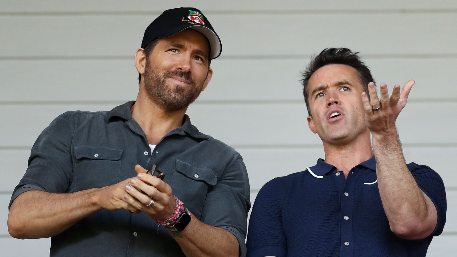 Ryan Reynolds and Rob McElhenney discuss Wrexham football club from the stands, showcasing team spirit and enthusiasm for the game.