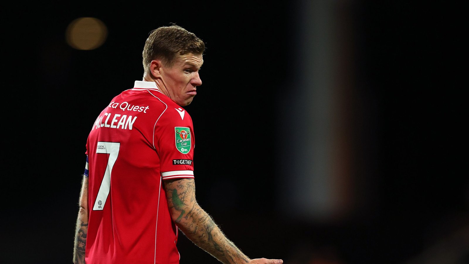 James McClean in het rode tenue van Wrexham met nummer 7, kijkend achterom tijdens een wedstrijd, met vastberadenheid en focus.
