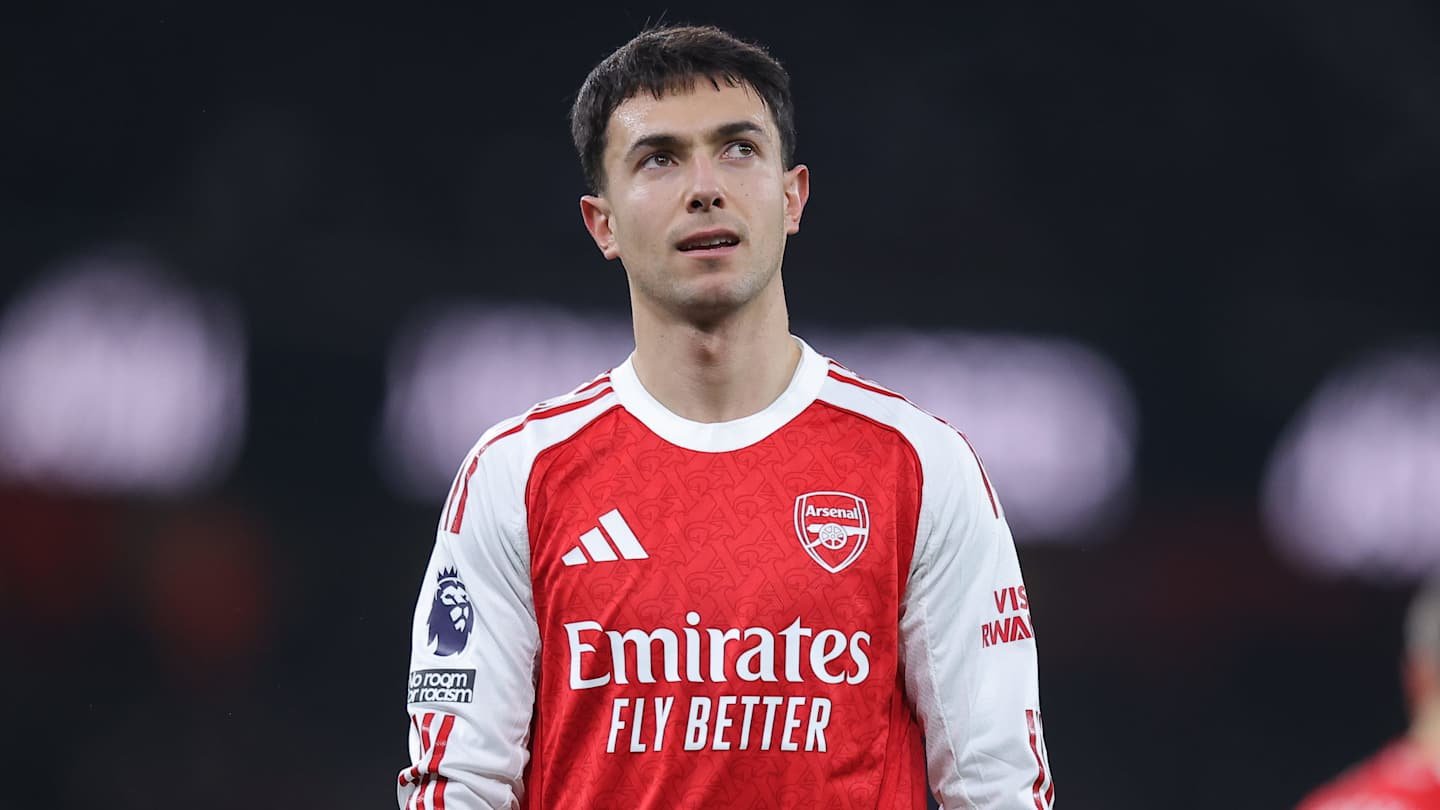Zubimendi in Arsenal's red home kit, looking thoughtful during a match, showcasing Premier League branding and club sponsorship.