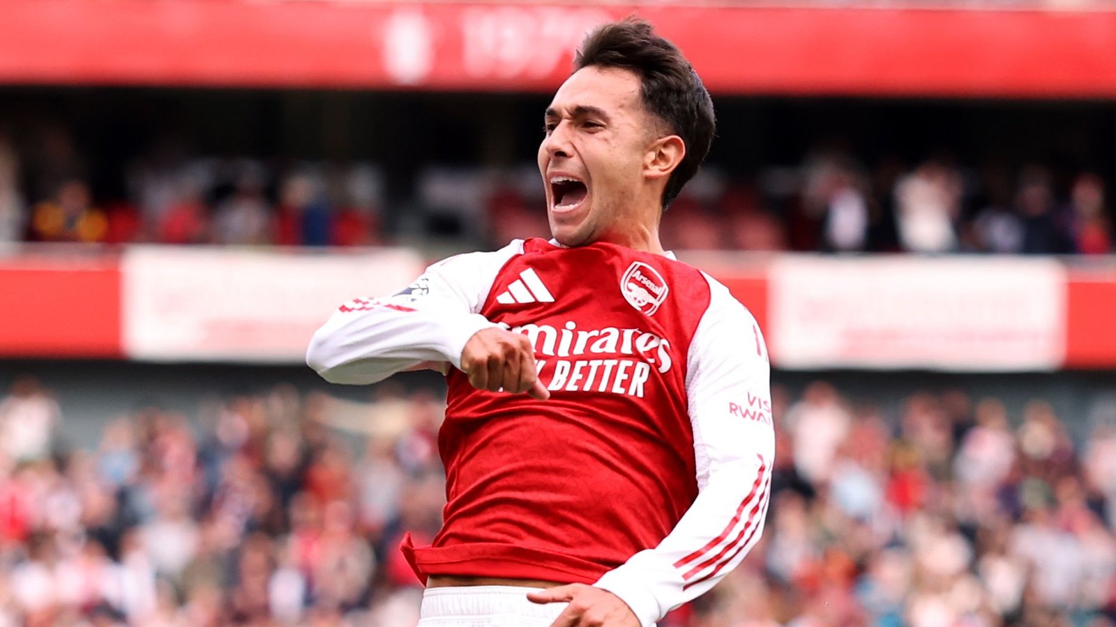Zubimendi celebrates a goal in Arsenal's red and white kit, showcasing his passion during a vibrant match atmosphere.