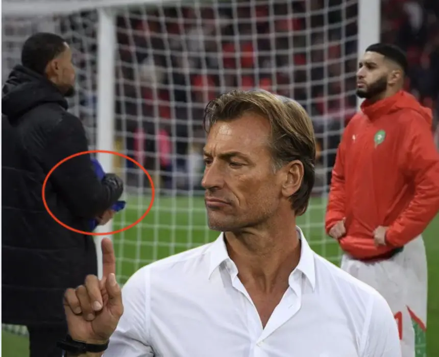 De coach van Marokko, Hervé Renard, gebaart bedachtzaam terwijl spelers op de achtergrond zich voorbereiden, wat de teamfocus voor een wedstrijd toont.