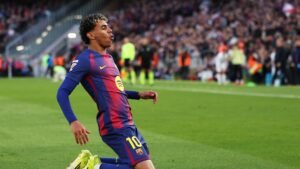 Barcelona player celebrating after scoring a goal, wearing the team's blue and claret kit, with fans cheering in the background.