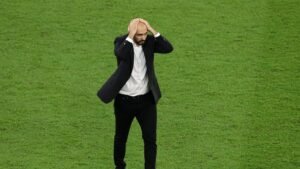 Walid Regragui shows visible frustration as he holds his head, standing on the lush green pitch during a tense moment in a match.