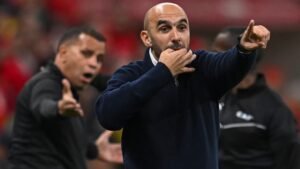 Walid Regragui gesturing passionately from the sidelines during a crucial match, with team staff in the background showing varied reactions.