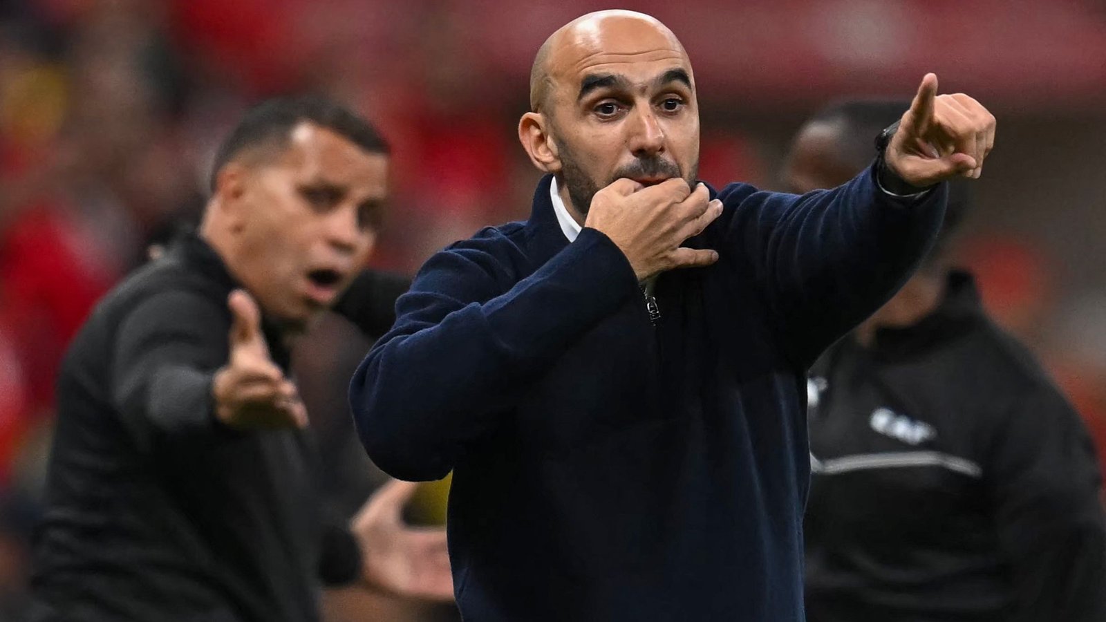 Walid Regragui gesturing passionately from the sidelines during a crucial match, with team staff in the background showing varied reactions.