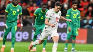 Moroccan player wearing jersey number 10 takes a penalty kick, with Senegalese defenders in green kit looking on in the background.