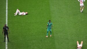 Moroccan players on the pitch, with several on the ground and a Senegalese player standing, during a competitive match.
