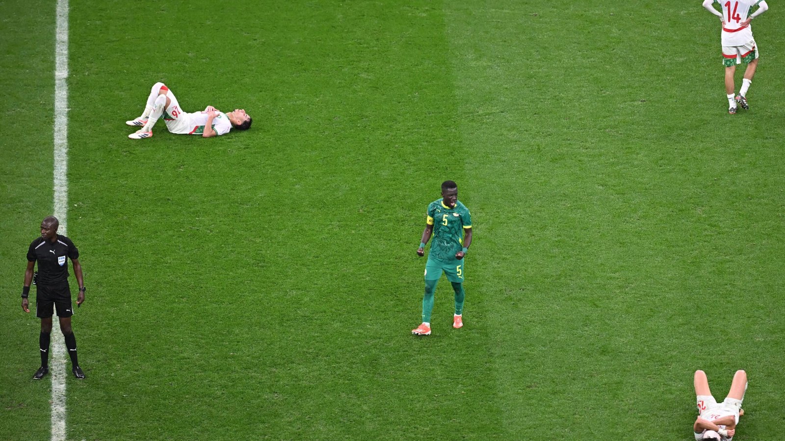 Moroccan players on the pitch, with several on the ground and a Senegalese player standing, during a competitive match.