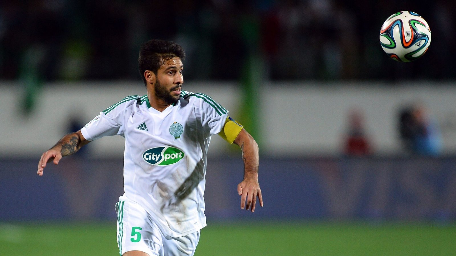 Mohsen Metwaly in action for Raja Casablanca, wearing a white kit with green accents, captaining his team during a match.