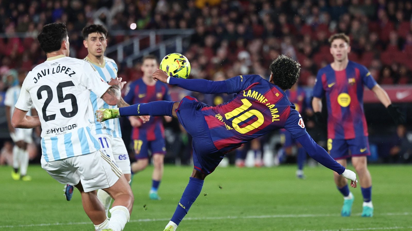 Lamine Yamal of Barcelona attempts a bicycle kick as Javi López defends, set against a vibrant stadium backdrop during a match.