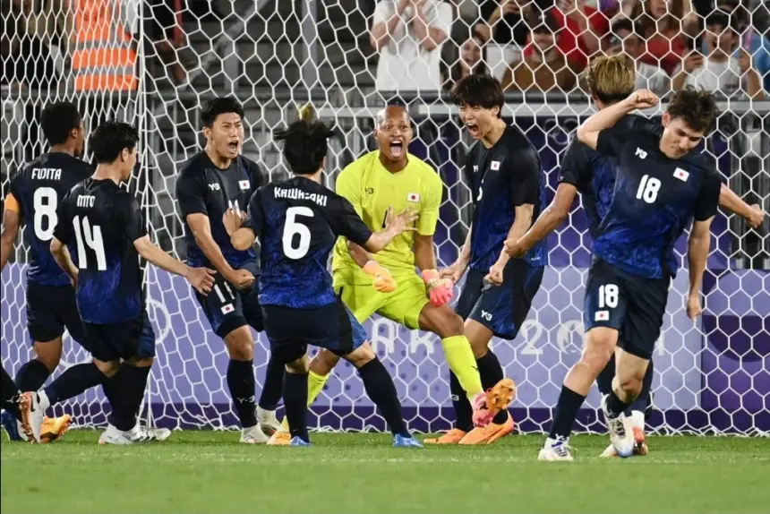 Japanse spelers vieren uitbundig na het scoren van een doelpunt, gekleed in levendige blauw-zwarte tenues, met de doelman in fel geel.