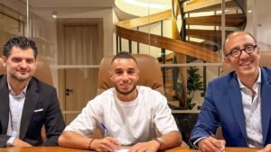 Walid Al Sheikh signs a contract with his new club, surrounded by officials in a modern office setting, smiling and engaged in discussion.