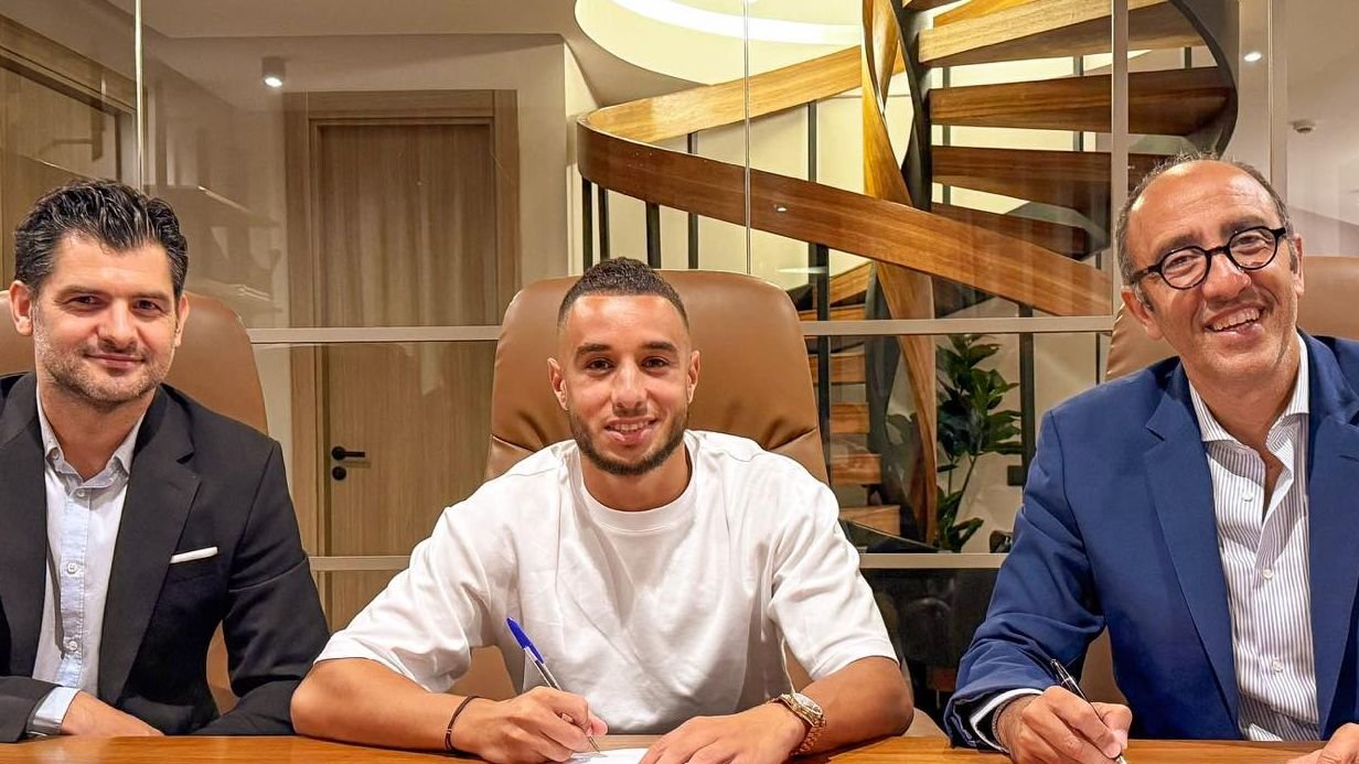 Walid Al Sheikh signs a contract with his new club, surrounded by officials in a modern office setting, smiling and engaged in discussion.