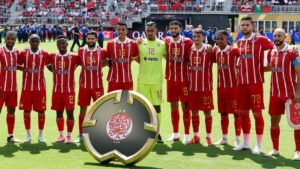 Wydad Casablanca players pose for a team photo in their red and white striped kit, showcasing the club’s emblem and a vibrant stadium backdrop.