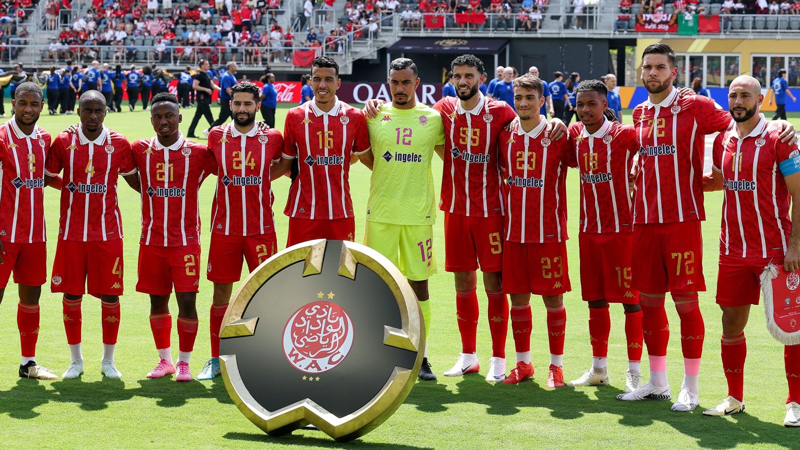 Wydad Casablanca players pose for a team photo in their red and white striped kit, showcasing the club’s emblem and a vibrant stadium backdrop.