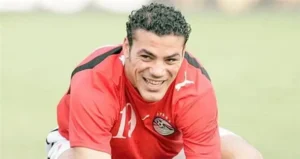 Ahmed Hegazy, wearing Egypt's red training kit, smiles while stretching during a training session on the pitch.
