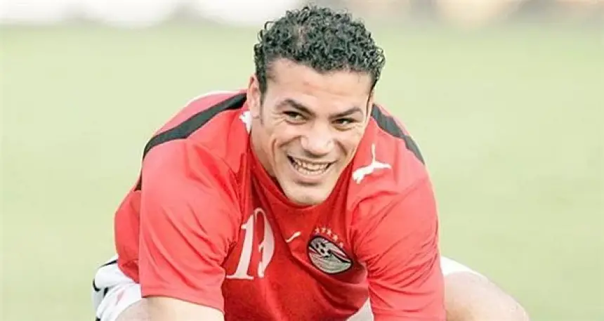 Ahmed Hegazy, wearing Egypt's red training kit, smiles while stretching during a training session on the pitch.