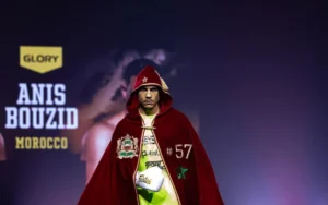 Anis Bouzid, Moroccan fighter, wears a red hooded cloak with the national emblem, walking towards the ring at a Glory event.