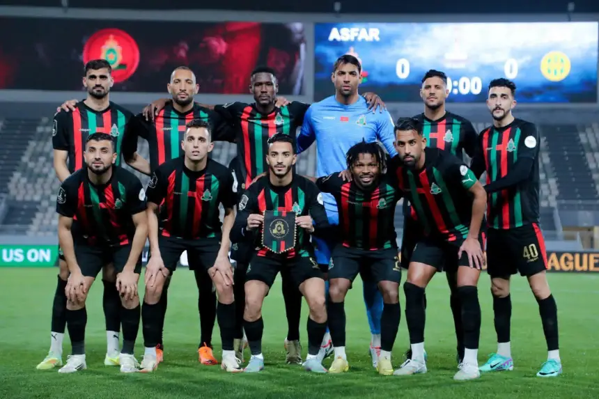 AS FAR-teamopstelling in zwart-rode tenues, poserend met een trofee; op de achtergrond een wedstrijd tegen CR Belouizdad, scorebord toont 0-0.