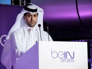 BeIN Sports spokesperson in traditional Qatari attire addresses the audience from a podium at a sports event, with a purple backdrop.