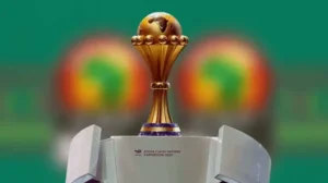 Le trophée de la Coupe d'Afrique des Nations est présenté avec un fond vert vif, symbolisant l'édition 2021 au Cameroun.