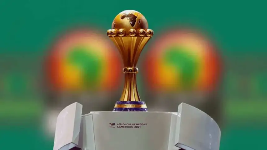 Le trophée de la Coupe d'Afrique des Nations est présenté avec un fond vert vif, symbolisant l'édition 2021 au Cameroun.