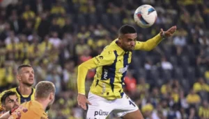 Youssef En-Nesyri leaps to head the ball during a match, wearing a yellow and blue kit, with opposition players in the background.