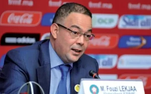 Fouzi Lekjaa, voorzitter van de FRMF, spreekt op een persconferentie, gekleed in een blauw pak en een bril, met een logo als achtergrond.