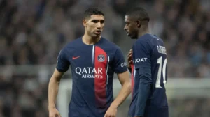 Achraf Hakimi en Ousmane Dembélé in PSG-tenues, bespreken tactieken tijdens een wedstrijd, waarbij hun teamwork en focus op het veld worden getoond.