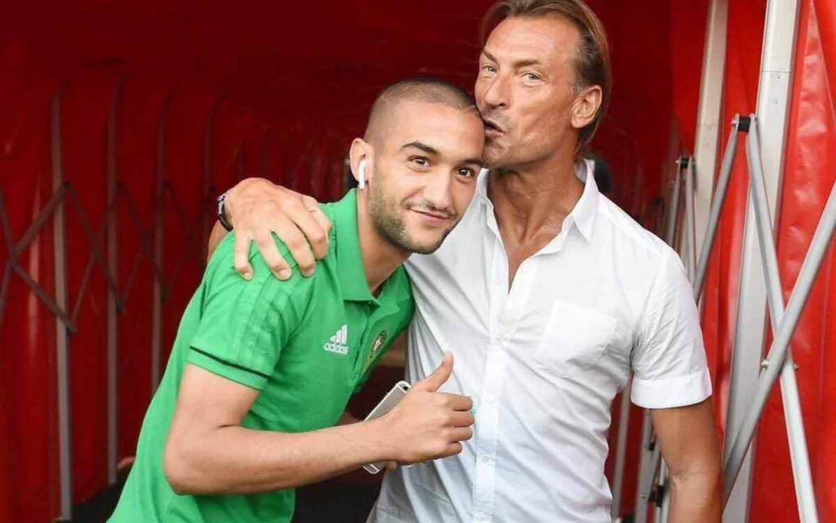 Hakim Ziyech in een groen Marokkaans tenue deelt een moment met coach Hervé Renard, beiden glimlachend in een rode tunnelomgeving.