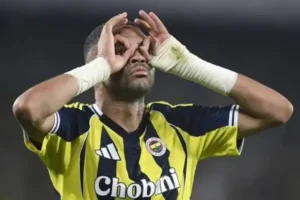 Fenerbahçe player celebrating with a playful gesture, wearing a yellow and navy striped jersey, during a match moment.