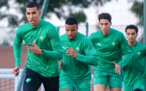 Spelers van het Marokkaanse nationale team sprinten in groene trainingspakken tijdens een trainingssessie, waarbij teamwork en voorbereiding worden getoond.