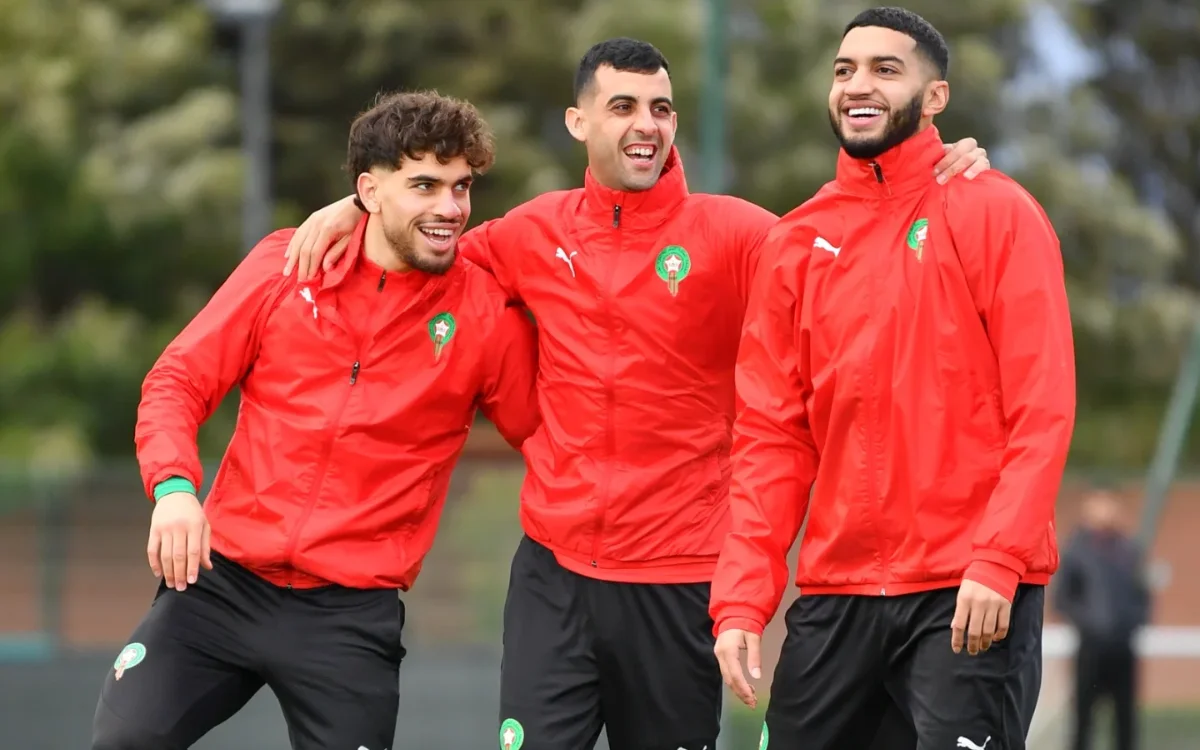 Moroccan national team players smiling together in training, wearing red jackets with green insignia, showcasing team camaraderie.