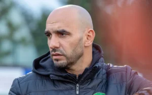 Walid Regragui, hoofdcoach van het Marokkaanse nationale voetbalelftal, lijkt diep in gedachten verzonken, gekleed in een zwart jasje, tijdens de training.