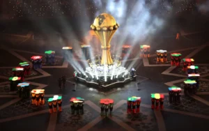 Feestelijk tafereel van de Afrika Cup 2028, met een gouden trofee omringd door levendige vlaggen van de deelnemende landen.