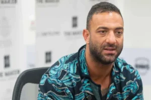 Mido, portant un maillot à motifs vibrants, assis pour une interview, démontrant son vif intérêt pour le football marocain.