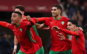 Moroccan players celebrate a goal with joy during a match against Ecuador, showcasing their vibrant red and green kit.