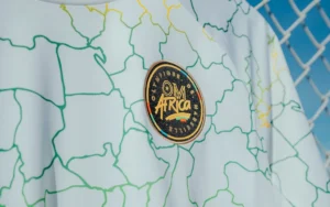 Olympique Marseille-shirt met een lichtblauwe achtergrond met een gestileerde kaart van Afrika in groen en geel, die de Marokkaanse voetbal benadrukt.