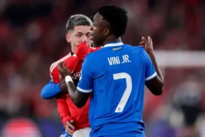 Vinícius Júnior in a blue jersey and a red-clad player embrace in celebration after a thrilling match, showcasing their camaraderie.
