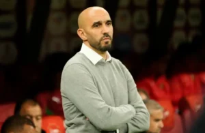 Walid Regragui observing from the sidelines, dressed in a grey sweater, during a tense moment in a Moroccan football match.
