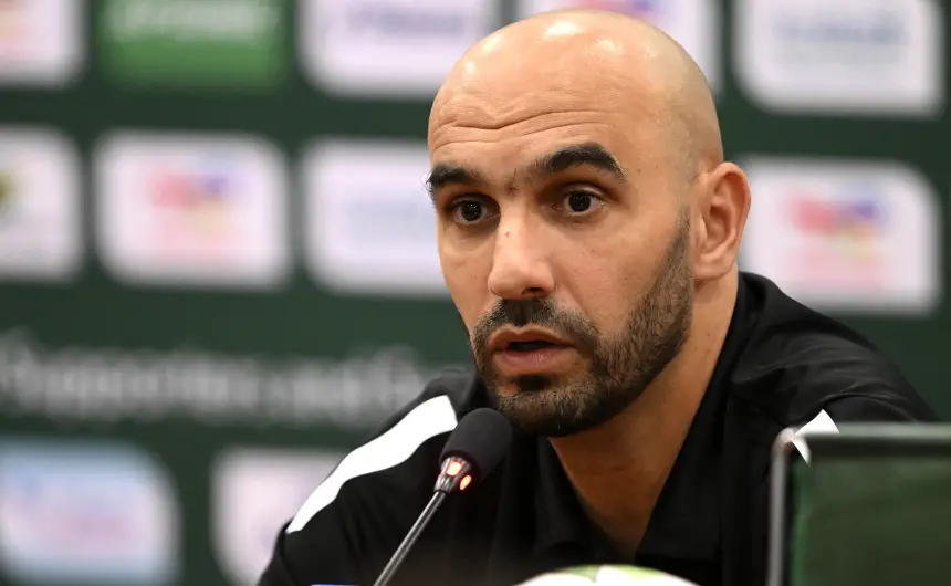 Walid Regragui speaks during a press conference, showcasing a focused expression against a green backdrop featuring sponsor logos.
